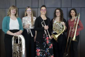 Members of the Magnolia Brass Quintet holding their instruments and smiling.