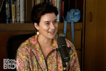 Rachel Spencer talking into a mic with a bookshelf behind her