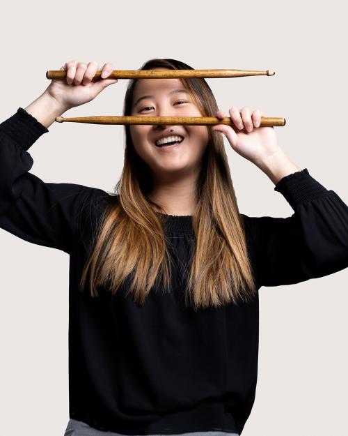Female Percussionist Looks through drumsticks and laughs 