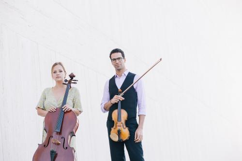 A female cellist and male violinist look into camera