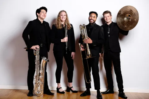 A group of Wind Symphony players holding instruments and laughing. 