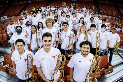 The Longhorn Pep Band smile into the camera fromt the basketball stadium stands