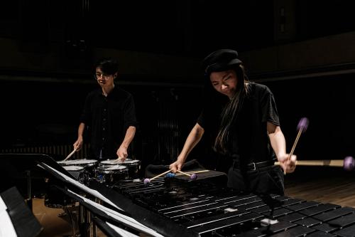 A marimba player and a snare drum player perform together at a Percussion Ensemble concert in a Darkened Bates Recital Hall
