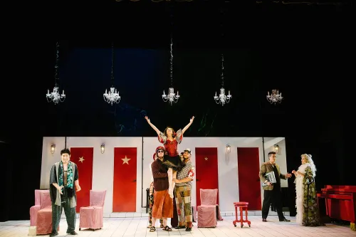 a group of castmates holds a starlet on their shoulders, while she sings, arms stretched out toward the sky.