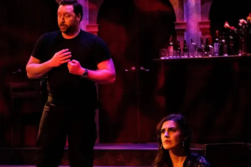 Carmen sits on the ground, ambivalently while a performer in a military uniform sings behind her.