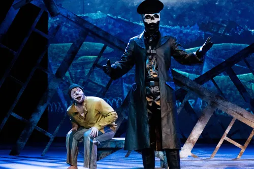 a performer dressed as death stands menacingly stage front, while a performer dressed as a mime cowers behind him.