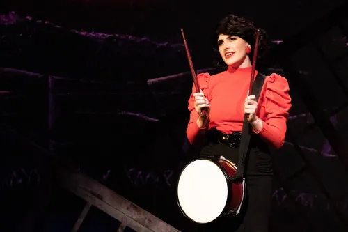 A performer in a red outfit plays a marching snare drum.