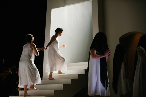 Two nuns wear only their undergarments. One leads the other up a staircase toward a bight white light, as if ascending into heaven.