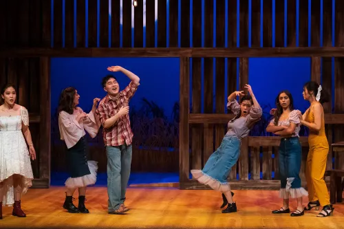 performers dance inside a barn set, during a party scene.