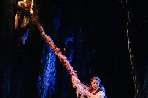 The Baker's wife tugs on the long braided hair of Rapunzel who is locked in a tower high above her on stage.