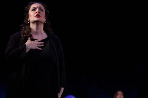 A woman holds one hand to her chest as she sings with her gaze lifted toward the sky.