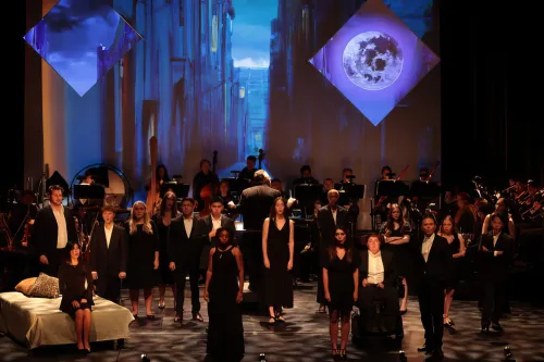 production still of a group of singers, clad in black, on a solemn stage