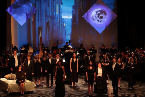 production still of a group of singers, clad in black, on a solemn stage