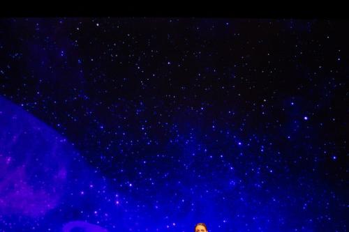 A singer and pianist perform on stage, behind a projection of a clear, starry night. High above them, the supertitles projection reads "Sleep, sleep, in they Sleep, little sorrows sit and weep."