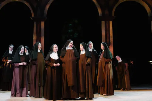 A group of nuns gather on the set of a monastery. 