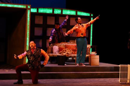 Three men perform on a stage aglow in neon lights.