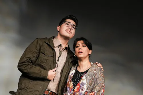 a man stands with his arm around a woman as they perform on stage.