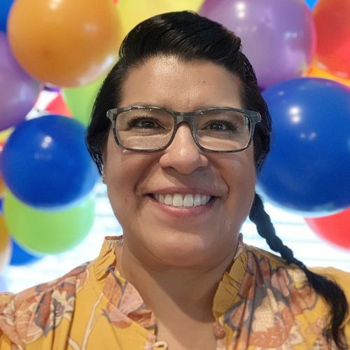 Delia Botbol Smiles for the camera in front of a wall of bright colorful balloons 