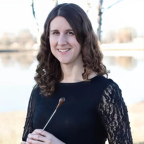 Laura Brock holds a conducting baton and smiles into camera