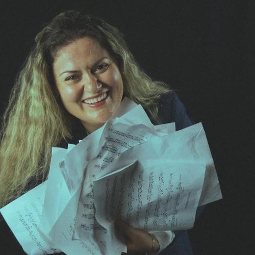 Ana Holds a chaotic and rumpled stack of sheet music as she smiles into the camera