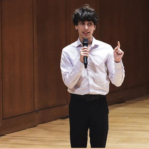 An image of Ethan Gurwitz, addressing an audience from the Bates Recital Hall stage