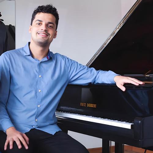 Headshot of Renan Branco, sitting at a grand piano and smiling into camera