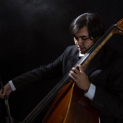 headshot of Gonzalo Kikuchi playing his bass in a dark room