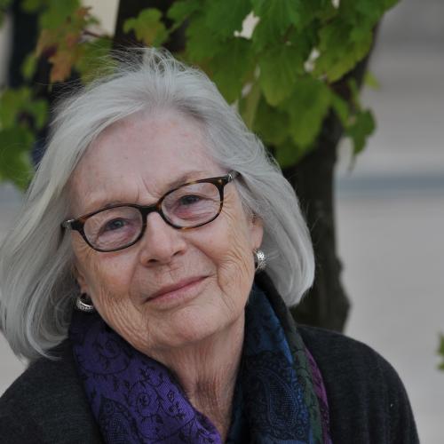 Emerita professor Judith Jellison sits outside in front of a tree smiling with wind blowing through her hair.