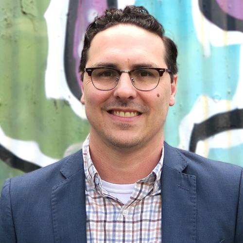 A headshot of Tony Rasmussen, standing against a colorful wall mural.