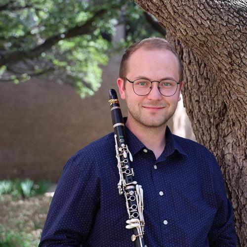 Jacob Bricker stands against a tree, holding his clarinet. 