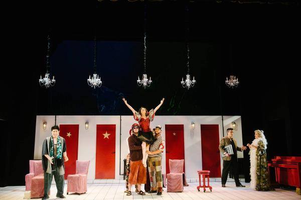a group of castmates holds a starlet on their shoulders, while she sings, arms stretched out toward the sky.