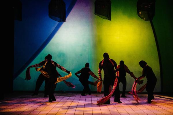 A group of dancer dressed in black from head to toe with even their faces covered, wrap long lengths of cloth around them as they dance on a dark, eerie stage.