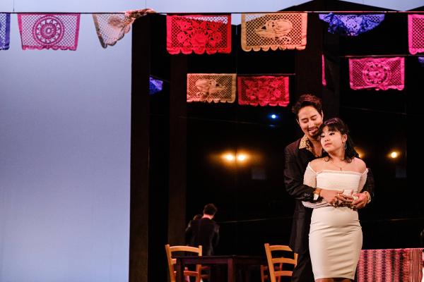 A man an woman sing in a loving embrace, at an outdoor cafe with festive party garlands hanging overhead.