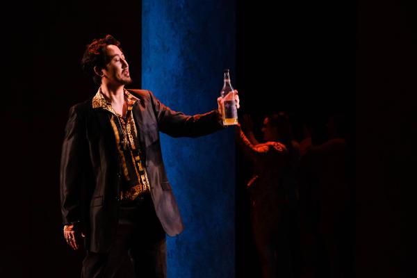 A man drinks from a liquor bottle as he sings solemnly. 