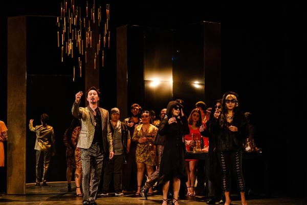 A group of partygoers lift shot glasses in a celebration toast amidst an ornate set gilded in gold.