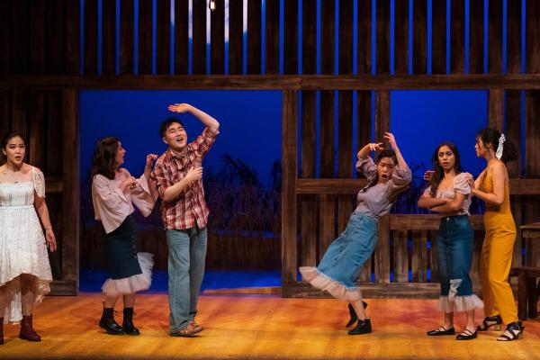 performers dance inside a barn set, during a party scene.