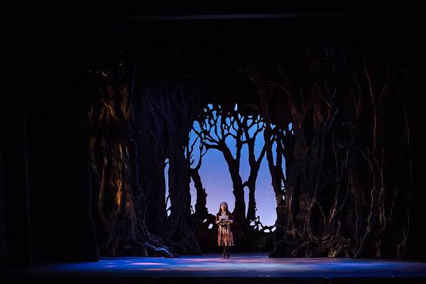 Gretel stands amid an epic forest set, holding a map and looking uncertain and frightened.