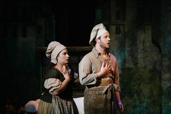 The Baker and his wife stand, staring off camera, each holding their hands to the hearts as if they are in disbelief.