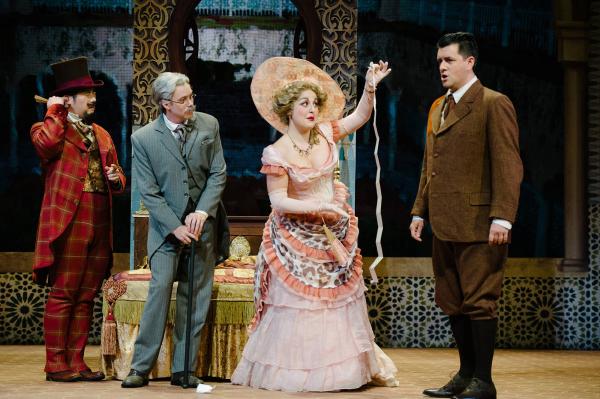 A woman in an ornate gown and hat holds a measuring tape up to a man in a brown suit. 