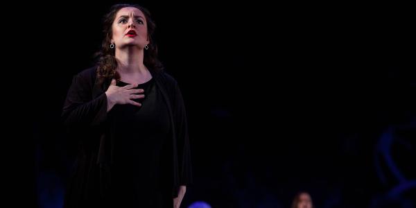 A woman holds one hand to her chest as she sings with her gaze lifted toward the sky.