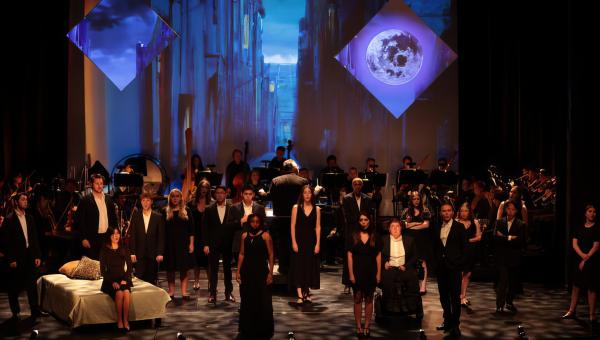 production still of a group of singers, clad in black, on a solemn stage