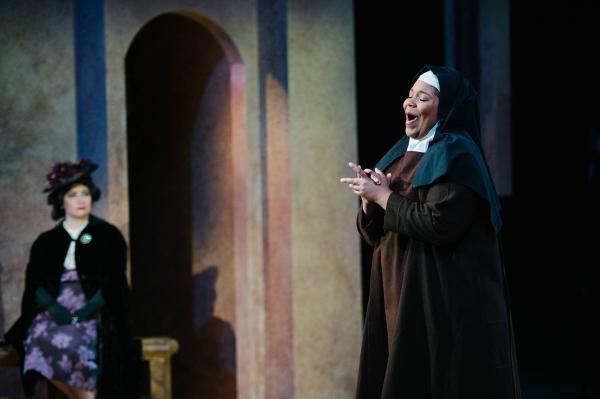 A nun sings passionatly as a woman in somber non-religious dress looks on from a nearby bench.