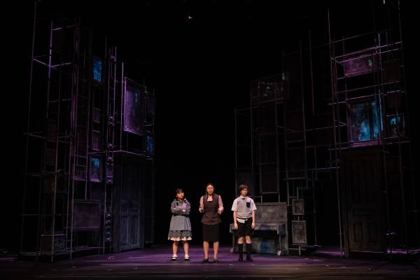 three performers stand center staged, dwarfed by a an expansive, ghostly gothic set