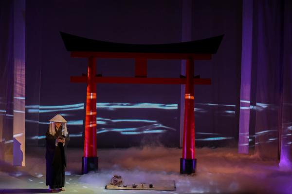 a shadowy figure stands on stage, at his feet is a traditional Chinese tea setting