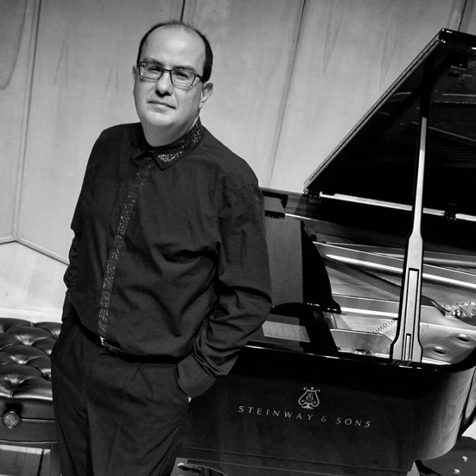 A headshot of Alexandre Dossin standing in front of a grand piano. 