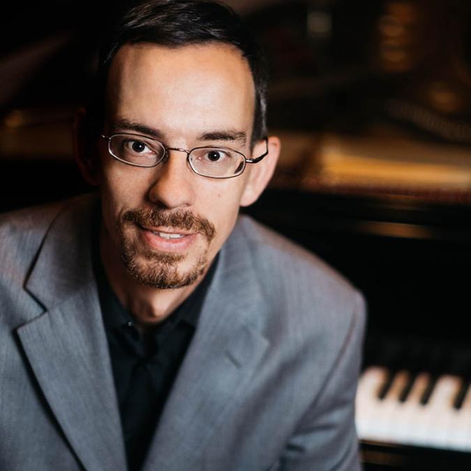 A headshot of Alexandre Maynegre-Torra, with a piano behind him.