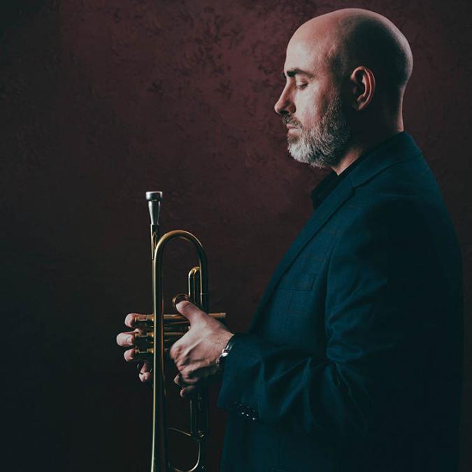 Side profile of Mike Sailors holding a trumpet with his eyes closed 