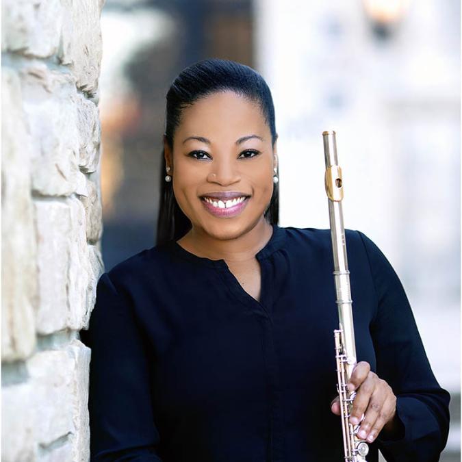 Ebonee Thomas stands against a limestone brick wall, holding her flute.