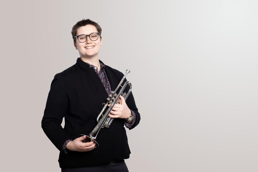 A trumpet player holds her trumpet and smiles