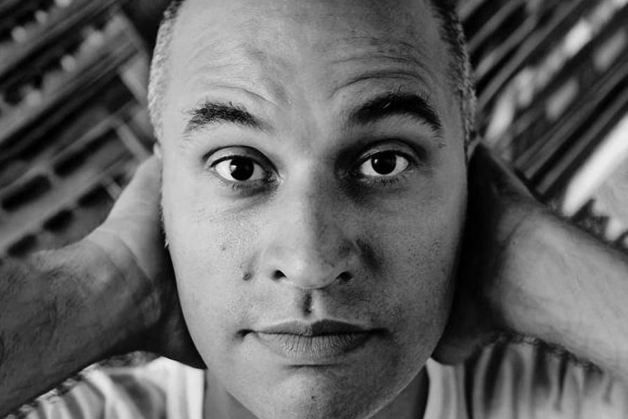 A close-up photo of a man raising his eyebrows with his hands behind his head.